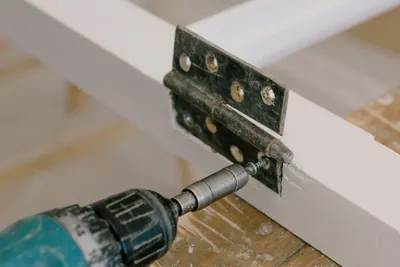 A cordless driver driving a screw into a hinge on a window frame