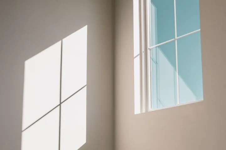 Sunlight through a window with glazing bars casting a grid onto a wall