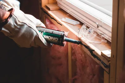 A gloved hand running a bead of caulk along a window seam